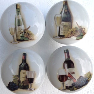 May include: Four ceramic cabinet knobs with a white background and a wine theme. Each knob features a bottle of wine, a glass of wine, and grapes. The bottles are labeled "Chateau Meursault" and "Wall Grand Cru".
