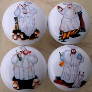 May include: Four white ceramic cabinet knobs with a chef design. Each knob features a different illustration of a chef in a white uniform, holding food or drink. The knobs have a glossy finish and are suitable for kitchen or dining room decor.