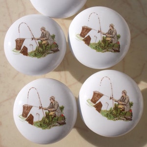 May include: Set of five white ceramic cabinet knobs with a fisherman with a fishing rod and a basket of fish design.