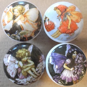 May include: Set of four ceramic knobs featuring whimsical fairy illustrations. Each knob depicts a fairy with wings, flowers, and a woodland background. The fairies are dressed in various colors, including pink, purple, red, and white.