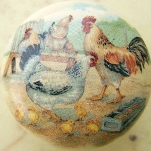 May include: A ceramic knob with a painted scene of a rooster, hens, and chicks in a barnyard setting. The rooster is red, white, and black, and the hens are white and black. The chicks are yellow.