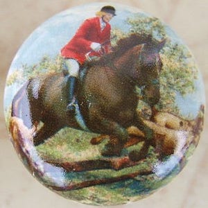May include: A ceramic knob with a vintage illustration of a rider on a brown horse jumping over a fence. The rider is wearing a red jacket and a black hat.