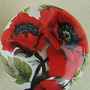 May include: Round decorative ceramic piece featuring a vibrant floral design. The artwork showcases large red poppies with black centers, green leaves, and a white background. The piece has a glossy finish.