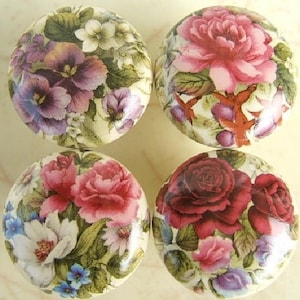 May include: Four round decorative knobs with floral designs. Each knob features a different arrangement of flowers, including roses, peonies, and pansies, in shades of pink, red, purple, and white, set against a cream-colored background.