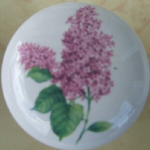 May include: A white ceramic knob with a purple lilac flower design. The knob has a glossy finish and is perfect for adding a touch of elegance to any room.
