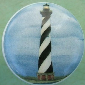 May include: A white and black striped lighthouse with a red roof against a blue sky background. The lighthouse is a popular symbol of the coast.