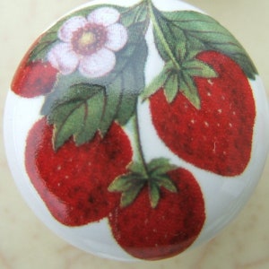 May include: A white ceramic knob with a painted design of red strawberries and a white flower with green leaves.