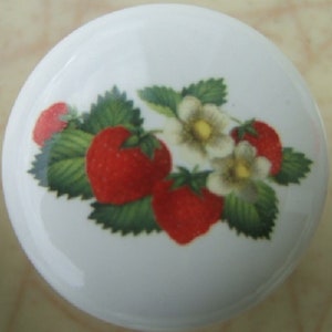May include: A white ceramic cabinet knob featuring a vibrant strawberry design. The knob showcases bright red strawberries, green leaves, and delicate white flowers with yellow centers, creating a fresh, summery aesthetic.