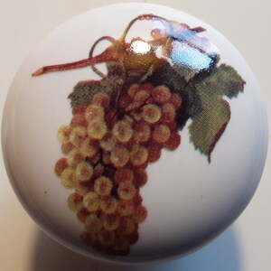 May include: A white ceramic knob with a printed image of a bunch of yellow grapes with green leaves.