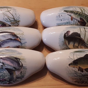 May include: Six white ceramic drawer pulls with a fish design. Each pull features a different type of fish, including a trout, a carp, a perch, and a pike.
