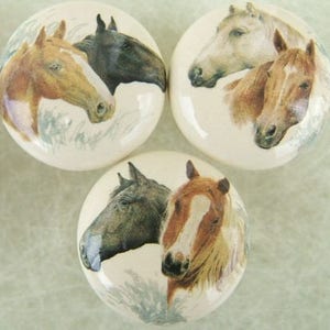 May include: Three ceramic knobs with images of horses. The knobs feature a brown and white horse, a black horse, and a white horse with a brown horse in the background.