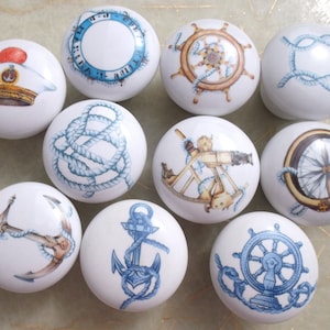 May include: Ten white ceramic knobs with nautical themed designs. The designs include a ship's wheel, an anchor, a compass, a sextant, a sailor's hat, and rope.