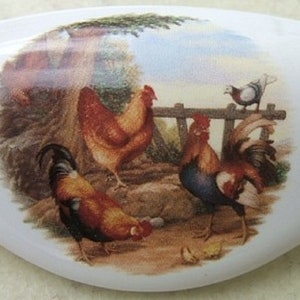 May include: White ceramic cabinet knob with a colorful image of three roosters and a dove in a barnyard setting. The image includes a tree, a fence, and a brown rock.