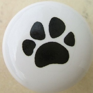May include: White, round cabinet knob with a black paw print design. The knob is glossy and features a simple, yet charming, pet-themed design. Ideal for adding a touch of personality to furniture or cabinetry.