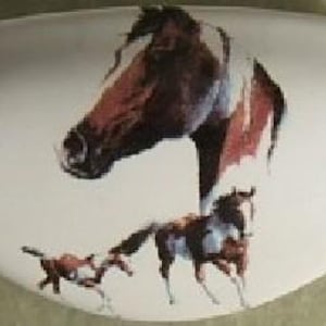 May include: White ceramic soap dish with a painted image of a brown and white horse and two smaller horses. The dish has a curved shape and a glossy finish. The horse image is detailed and realistic.