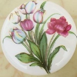 May include: A round, white ceramic knob featuring a floral design. The design includes a bouquet of tulips in shades of pink, purple, and white, with green leaves and stems. The knob has a glossy finish.
