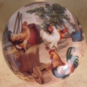 May include: A round, ceramic knob with a painted image of a rooster, hens, and a tree. The knob is brown with a glossy finish.