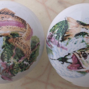 May include: Two white ceramic ornaments with a painted design of fish. The fish are brown, orange, and pink with green and blue foliage.