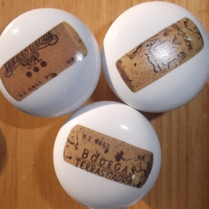 May include: Three white ceramic knobs with cork labels. The labels feature the text "Bodegas Terras Gauda", "Terra Gauda", and "Bodegas", respectively.