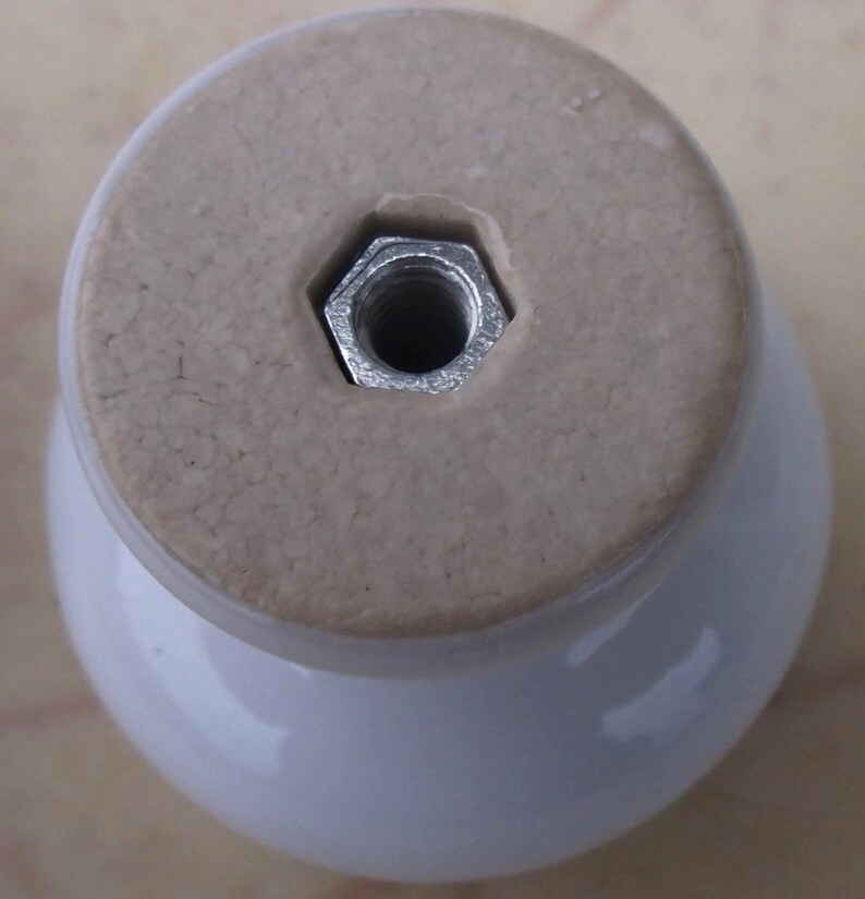 May include: White ceramic knob with a silver metal threaded insert. The knob has a smooth, rounded top and a slightly textured base.