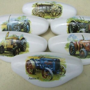 May include: Set of 6 white ceramic drawer pulls with vintage tractor designs. Each pull features a different tractor model with its name printed below. The tractors are depicted in a colorful, cartoon style.