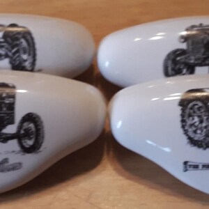 May include: Set of four white ceramic drawer pulls with black and white images of vintage tractors. The pulls feature the text "The Farmer Tractor" and "Fordson" on them.