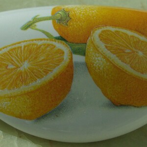 May include: A white ceramic dish with a painted design of three lemons. The lemons are yellow with a light brown stem and green leaves.