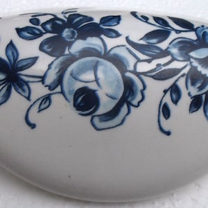 May include: White ceramic drawer pull with a blue floral design. The oval-shaped pull features a detailed pattern of blue flowers and leaves, adding a touch of elegance to any cabinet or drawer. The pull measures approximately 5 inches in length.