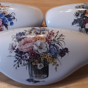 May include: Three white ceramic drawer pulls with floral designs. Each pull features a bouquet of colorful flowers in a vase.