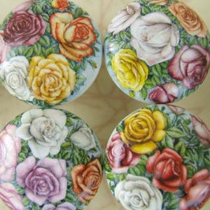 May include: Four round cabinet knobs with a floral design. Each knob features a different arrangement of roses in shades of red, yellow, white, and purple, surrounded by green leaves, set against a light blue background.
