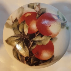 May include: A white ceramic knob with a painted design of red apples and green leaves.