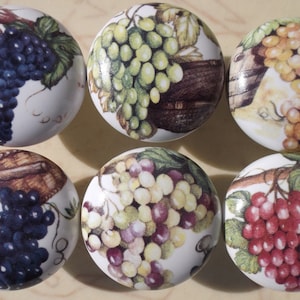May include: Six ceramic knobs with a white background and a grape design. The grapes are in various colors, including green, purple, and red. The knobs are perfect for adding a touch of rustic charm to any kitchen or bathroom.