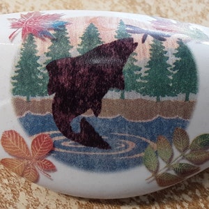 May include: White ceramic knob with a colorful design of a fish jumping out of the water, surrounded by trees and leaves.