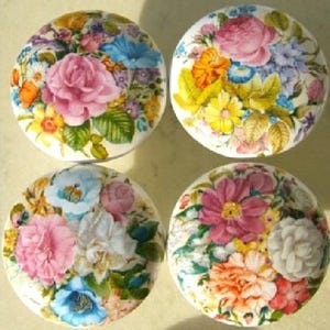 May include: Four round decorative cabinet knobs with floral designs. Each knob features a different arrangement of colorful flowers, including pink roses, blue blossoms, and yellow accents, set against a white background. These knobs add a touch of vintage charm.