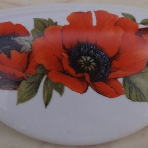 May include: White ceramic decorative piece with a curved shape, adorned with a vibrant floral design. The design features three red poppies with black centers and green leaves, creating a striking contrast.