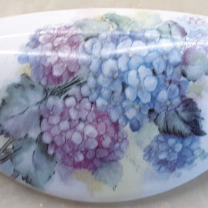 May include: A white ceramic drawer pull with a painted design of purple and blue hydrangeas with green leaves.