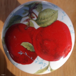 May include: White ceramic knob with a red apple design. The knob features two red apples with green leaves and a white background.