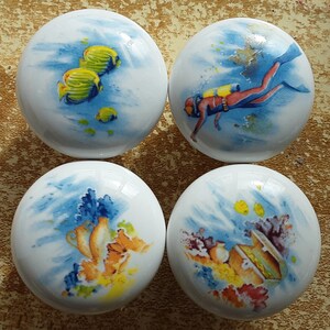 May include: Four ceramic knobs with different underwater scenes. One knob features yellow fish, another has a scuba diver, and the other two have coral reefs and treasure chests.