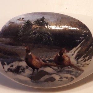 May include: White ceramic dish with a round image of two pheasants in a snowy forest scene.