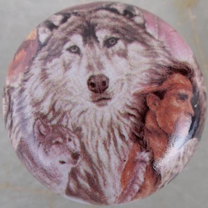 May include: A round decorative cabinet knob featuring a detailed image of a wolf's face, with a second wolf and a person in the background. The knob has a glossy finish and a color palette of brown, white, and pink.