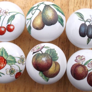 May include: Six white ceramic knobs with different fruit designs. Each knob features a different fruit, including cherries, strawberries, pears, plums, apples, and peaches.