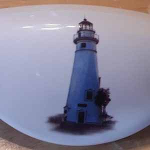 May include: White ceramic dish with a blue and white lighthouse design. The dish features three lighthouses, each with a white tower and a blue base.