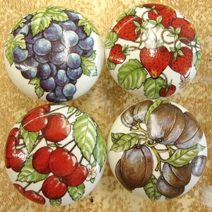 May include: Four round ceramic cabinet knobs with fruit designs. The knobs feature images of grapes, strawberries, cherries, and plums. Each knob has a white background with colorful fruit illustrations and green leaves.