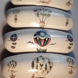 May include: Set of four white ceramic drawer pulls with a whimsical hot air balloon design. Each pull features a different balloon with various colors and patterns, including green, blue, red, and white.