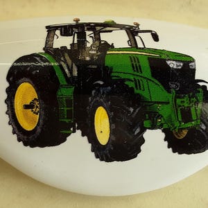 May include: A green and black tractor with yellow wheels on a white ceramic tile.