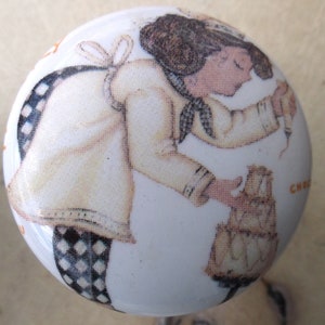 May include: A white ceramic knob with a black and white checkered pattern. A girl in a white dress with a black bow is holding a cake.