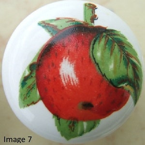 May include: A white ceramic knob with a red apple and green leaves painted on it. The apple has a white highlight on the side.