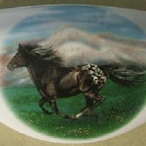 May include: A white ceramic trinket dish with a painted image of a brown and white horse running through a green field with a mountain in the background.