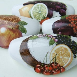 May include: A collection of decorative, oval-shaped stones, each featuring a vibrant, realistic depiction of various fruits. The stones showcase images of apples, cherries, grapes, oranges, lemons, and other fruits, creating a colorful display.