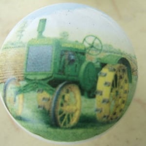 May include: A green and black tractor with a white background. The tractor has a large front tire and a smaller back tire. The tractor is in a field of green grass.